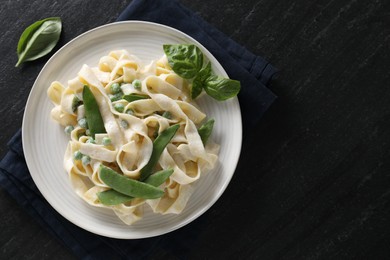 Photo of Delicious pasta with green peas and creamy sauce on black table, top view. Space for text