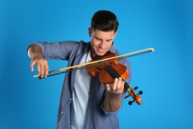 Happy man playing violin on light blue background
