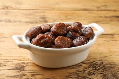 Photo of Roasted edible sweet chestnuts in dish on light wooden table