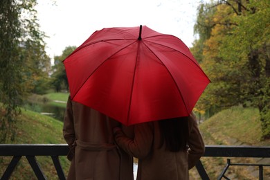 Photo of Couple with red umbrella in autumn park, back view