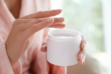 Photo of Woman with jar of moisturizing cream on blurred background, closeup