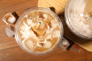 Photo of Refreshing iced coffee with milk in takeaway cups on wooden table, flat lay