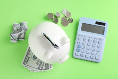 Financial savings. Piggy bank, dollar banknotes, coins and calculator on green background, flat lay