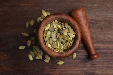Photo of Mortar with pumpkin seeds and pestle on wooden table, flat lay