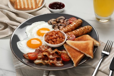 Plate of fried eggs, mushrooms, beans, tomatoes, bacon, sausages and toasts served on white marble table, closeup. Traditional English breakfast