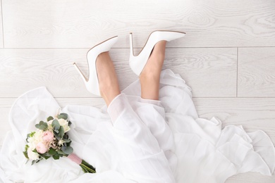 Photo of Young bride with bouquet wearing classic wedding shoes indoors, top view