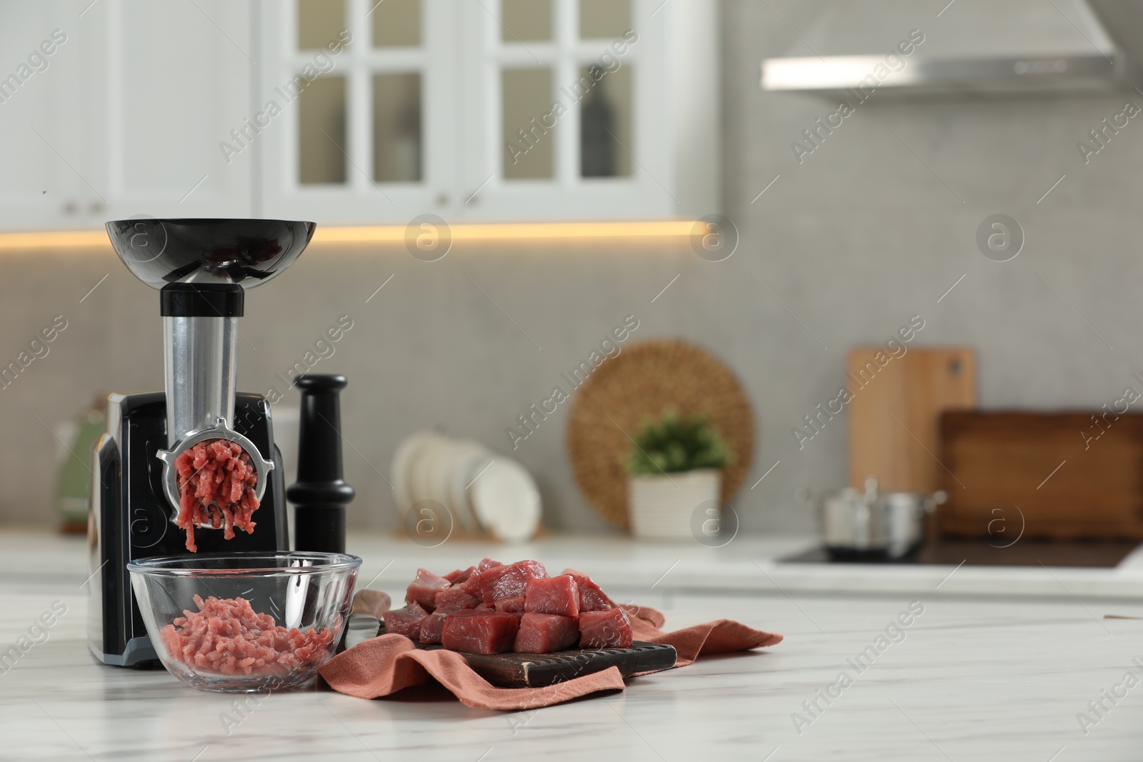 Photo of Electric meat grinder with beef mince on white table in kitchen, space for text