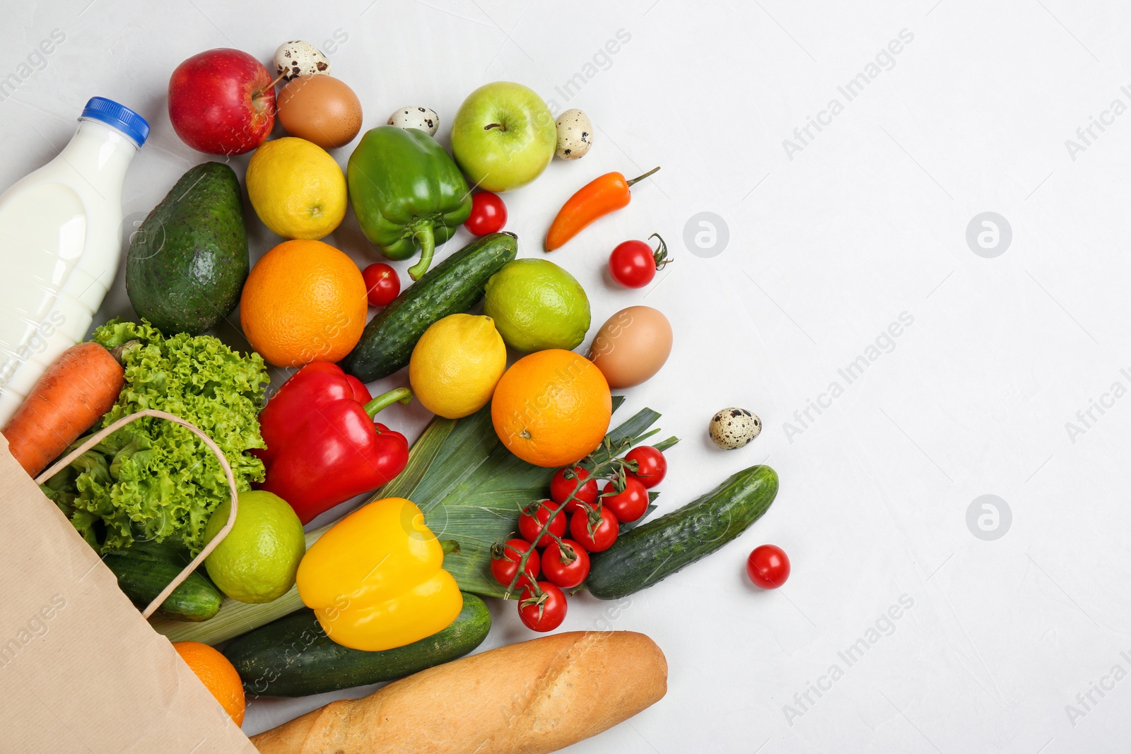 Photo of Flat lay composition with overturned paper bag and groceries on white table