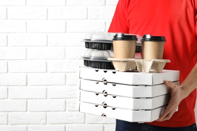 Photo of Courier with stack of orders near white brick wall, space for text. Food delivery service