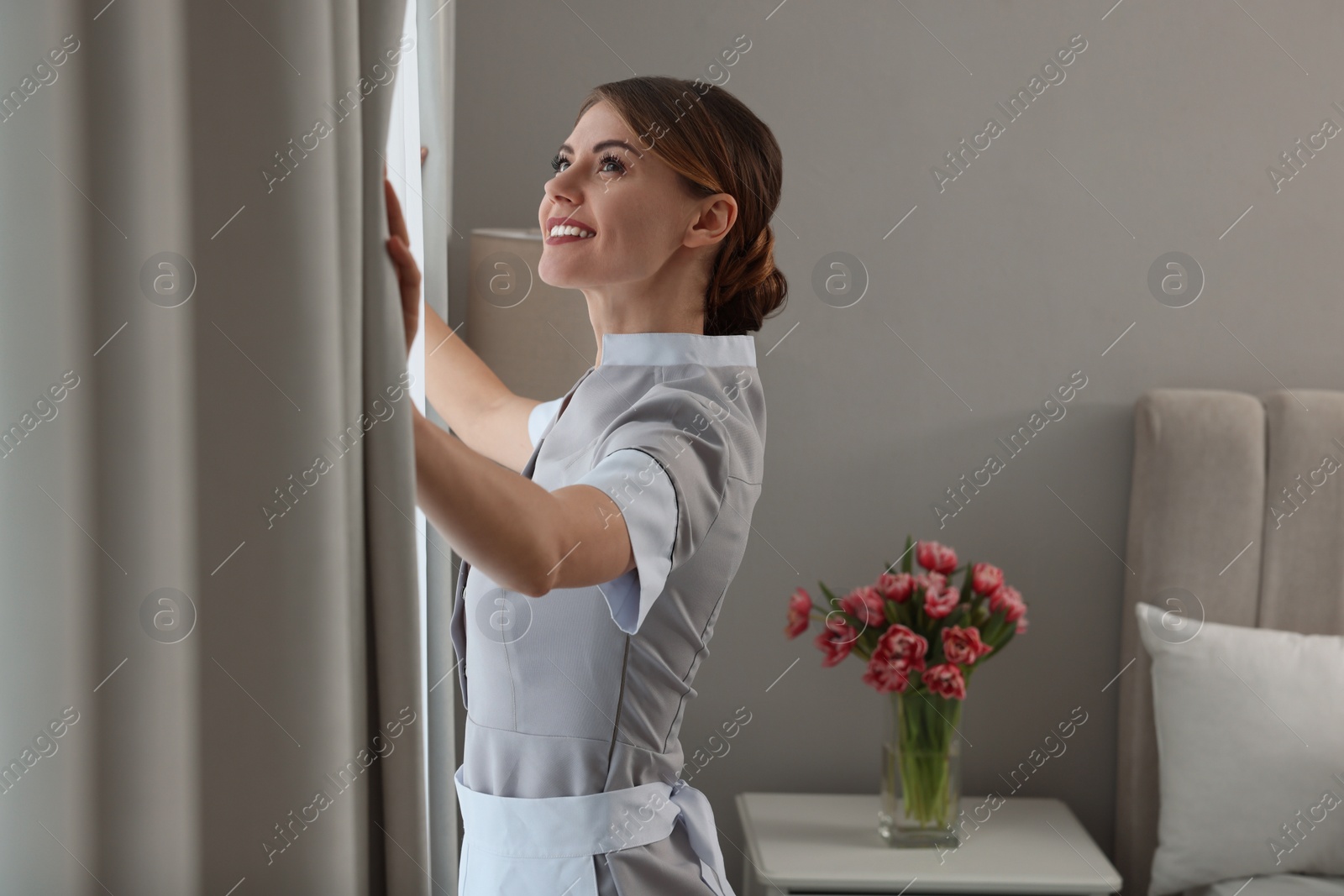 Photo of Chambermaid opening window curtains in hotel bedroom