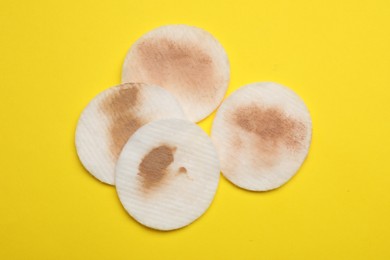 Photo of Dirty cotton pads after removing makeup on yellow background, flat lay