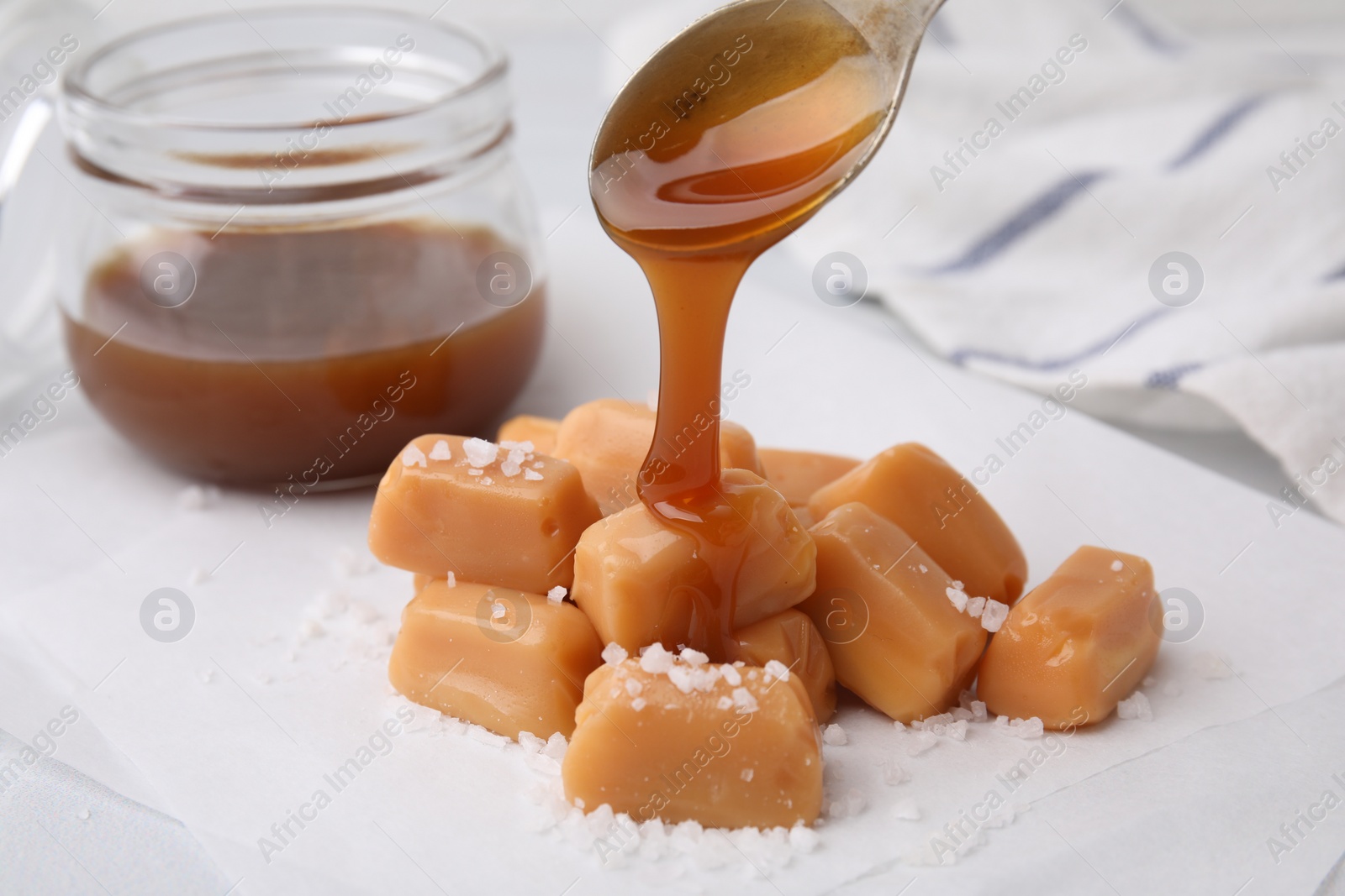 Photo of Pouring delicious salted caramel on candies on white table