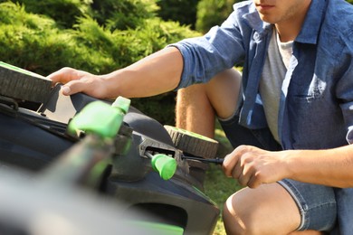 Young man with screwdriver fixing lawn mower in garden, closeup