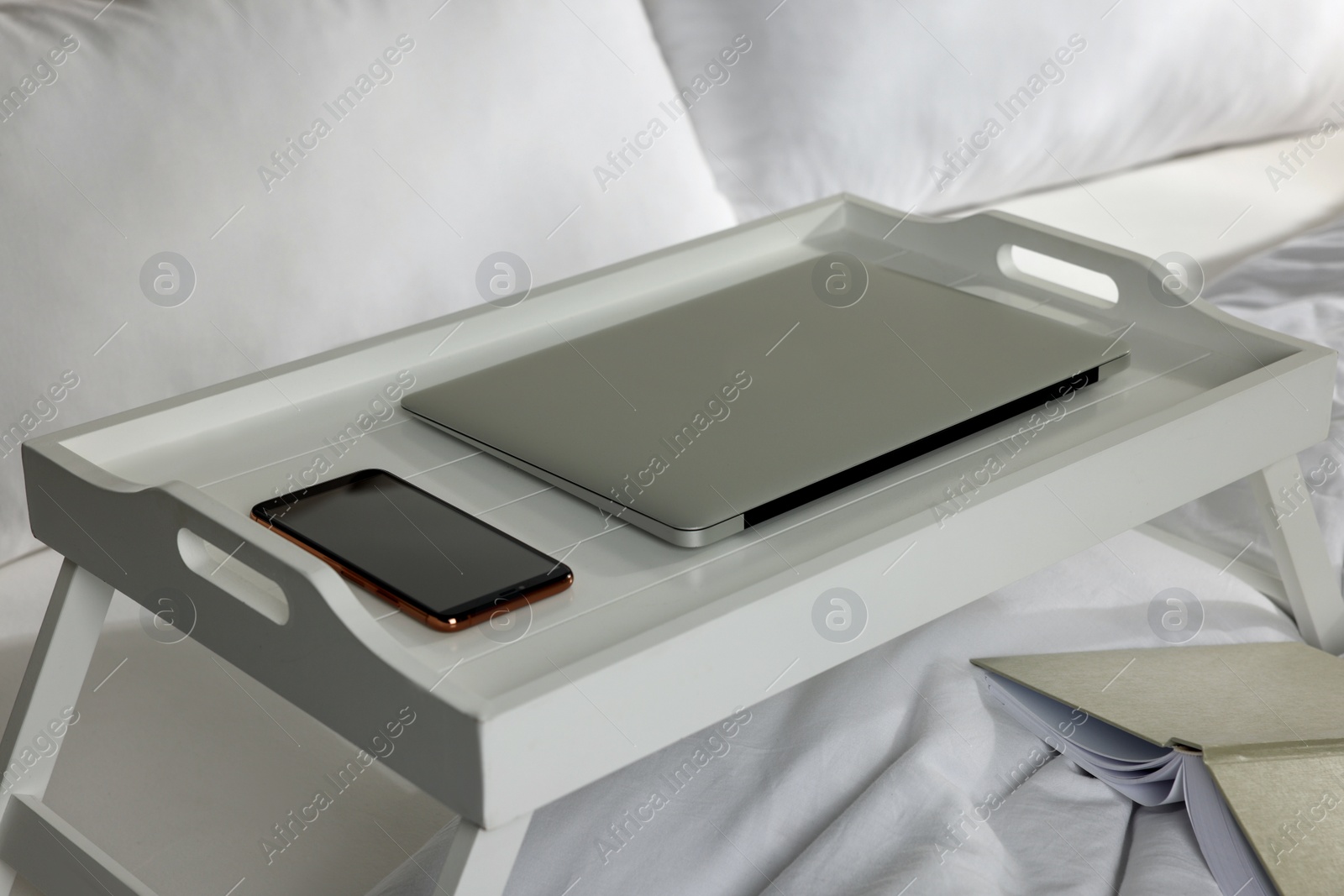 Photo of White tray with modern laptop and smartphone on bed indoors