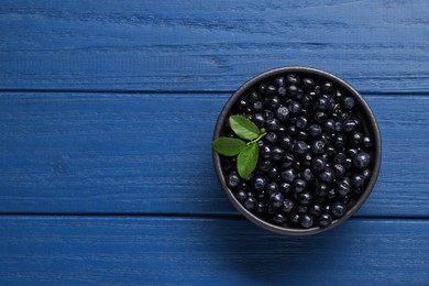 Photo of Tasty fresh bilberries with green leaves in bowl on blue wooden table, top view. Space for text