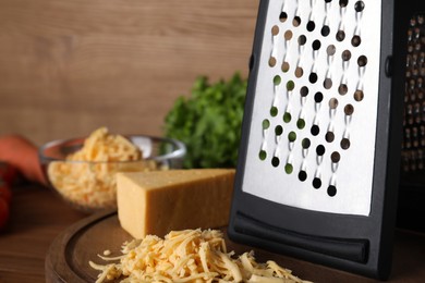 Photo of Grater and delicious cheese on wooden board, closeup