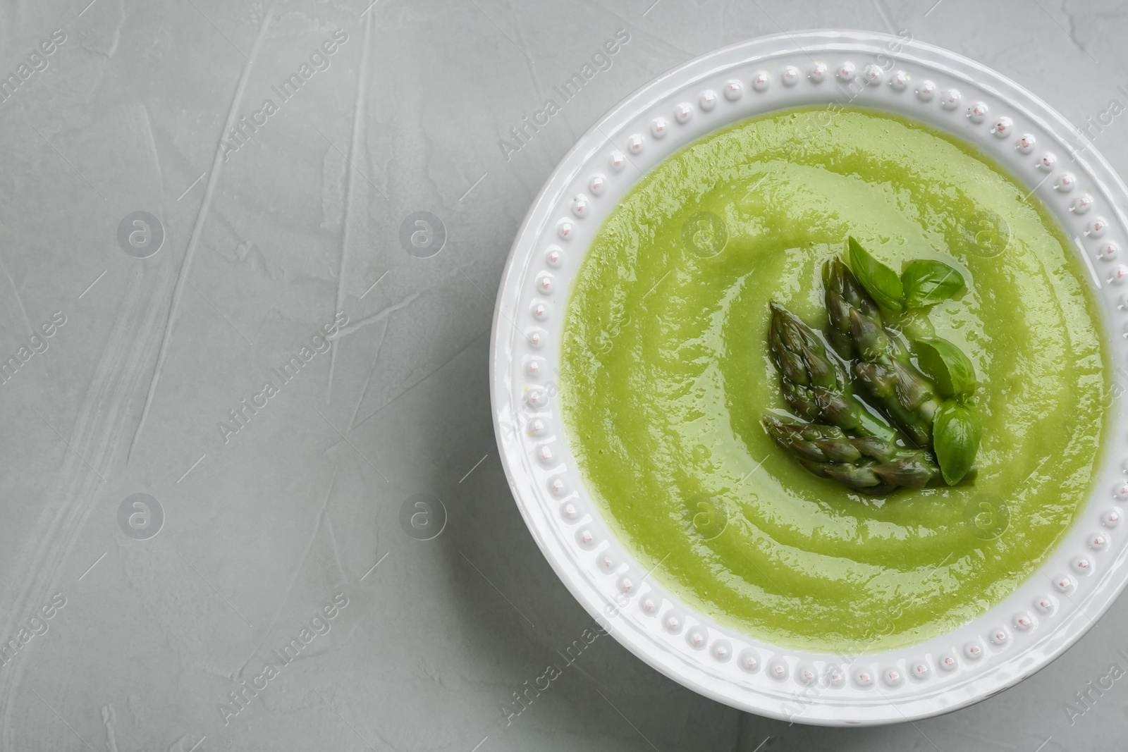 Photo of Delicious asparagus soup on grey table, top view. Space for text