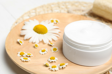 Jar of cream and chamomiles on wooden plate, closeup