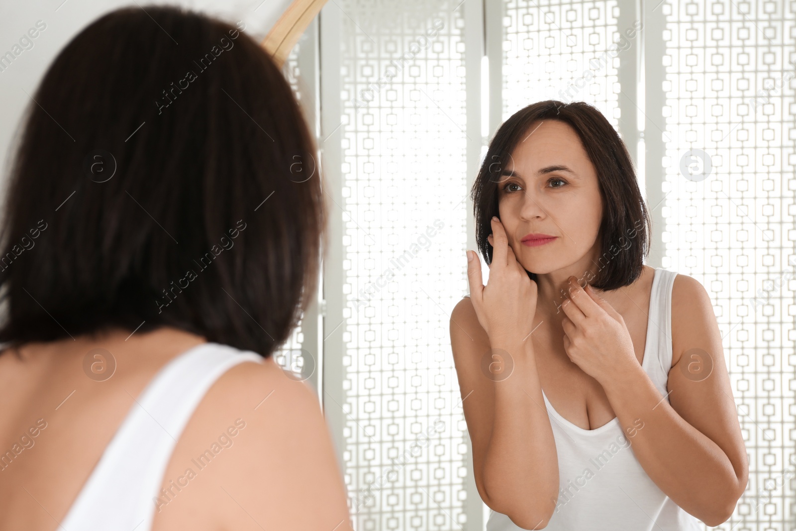 Photo of Beautiful mature woman with clean skin looking at mirror in bathroom