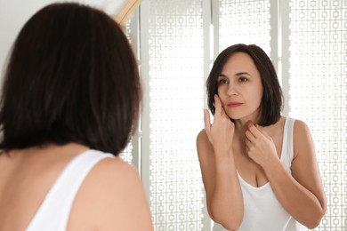 Photo of Beautiful mature woman with clean skin looking at mirror in bathroom