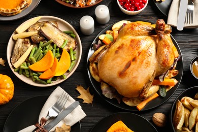 Traditional Thanksgiving day feast with delicious cooked turkey and other seasonal dishes served on black wooden table, flat lay