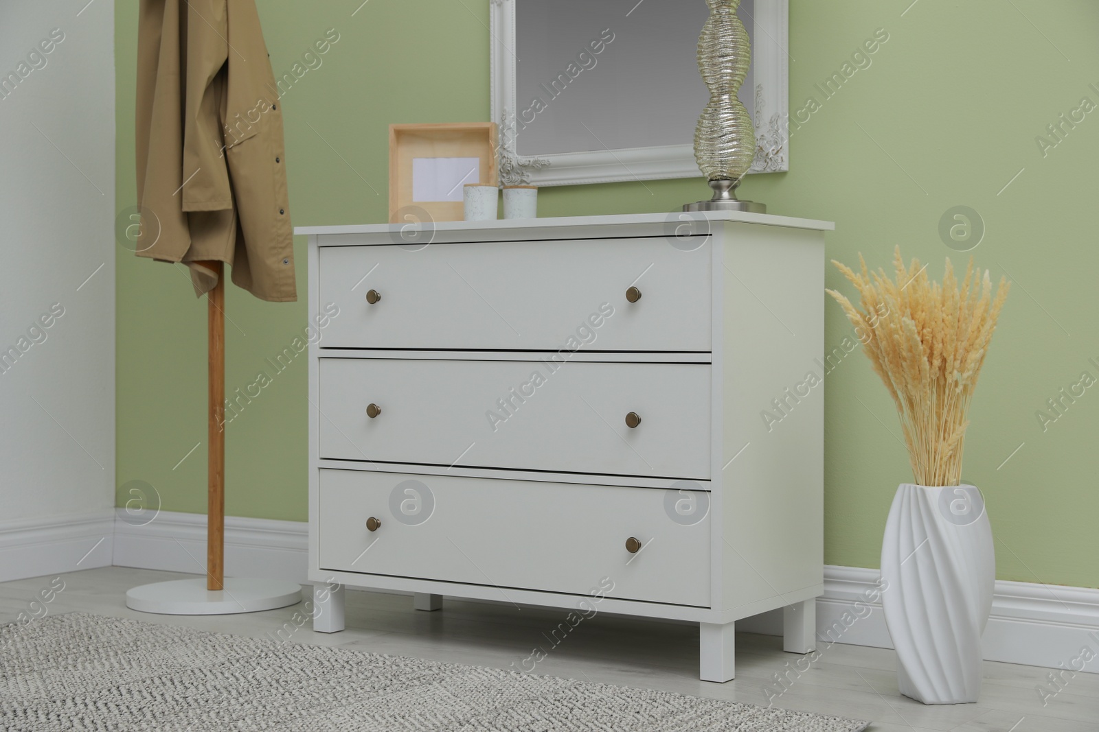 Photo of White chest of drawers with decor, coat stand and mirror in hallway. Interior design