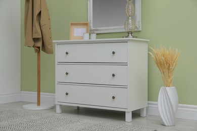 White chest of drawers with decor, coat stand and mirror in hallway. Interior design