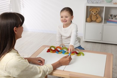 Photo of Motor skills development. Mother helping her daughter to play with colorful wooden arcs at white table in room