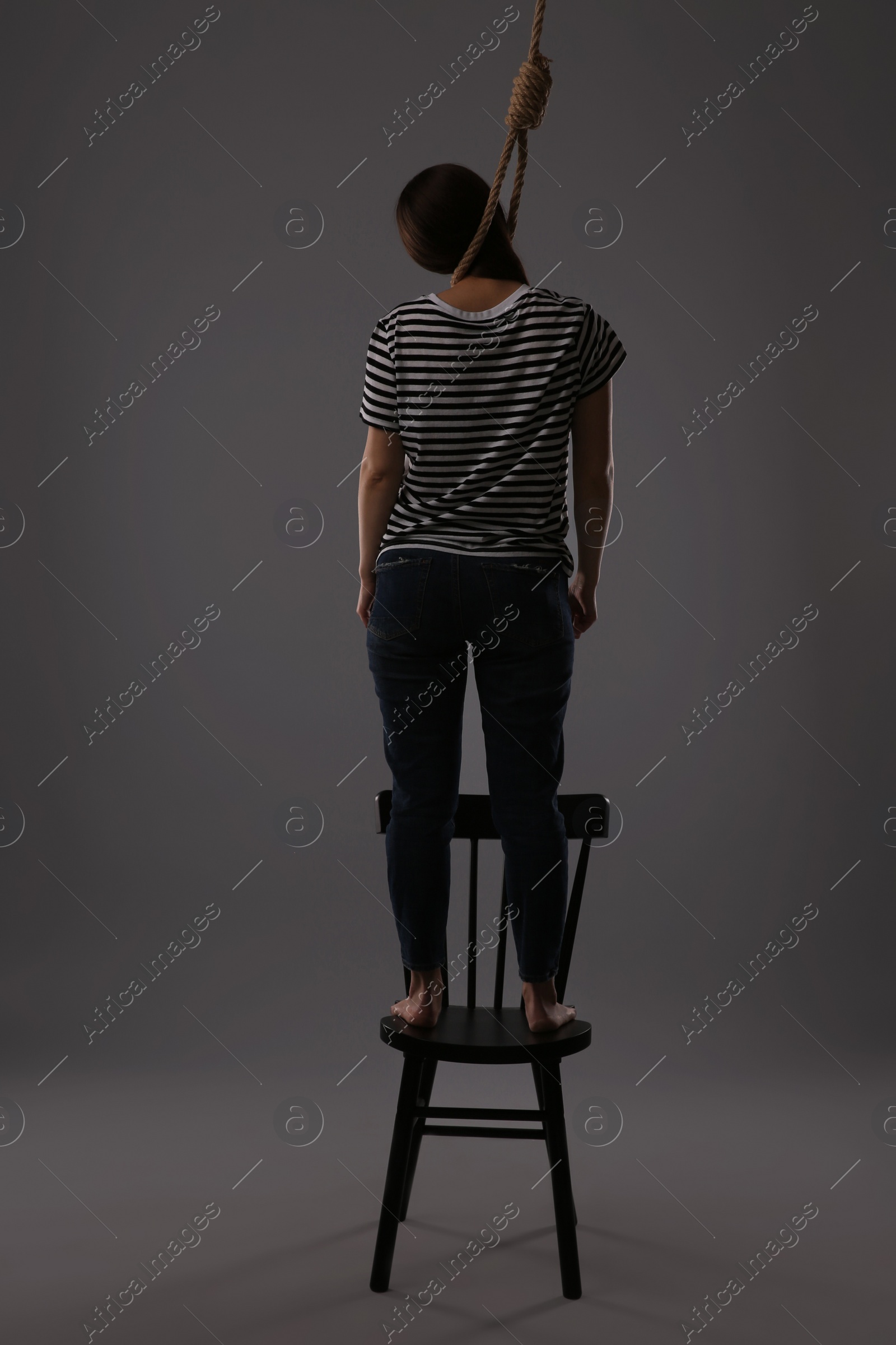 Photo of Woman with rope noose standing on chair against grey background, back view