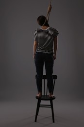 Woman with rope noose standing on chair against grey background, back view