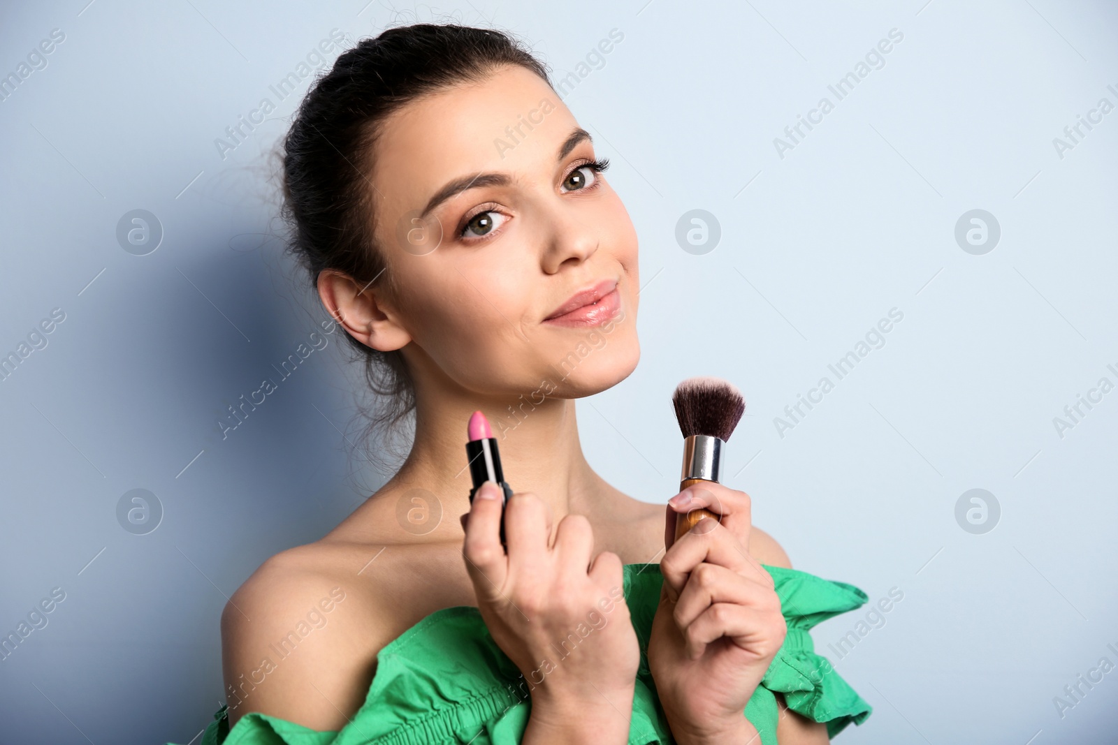 Photo of Young woman with lipstick and makeup brush on color background. Professional cosmetic products