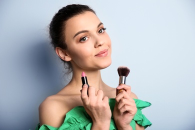 Young woman with lipstick and makeup brush on color background. Professional cosmetic products