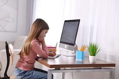 Photo of E-learning. Girl taking notes during online lesson at table indoors