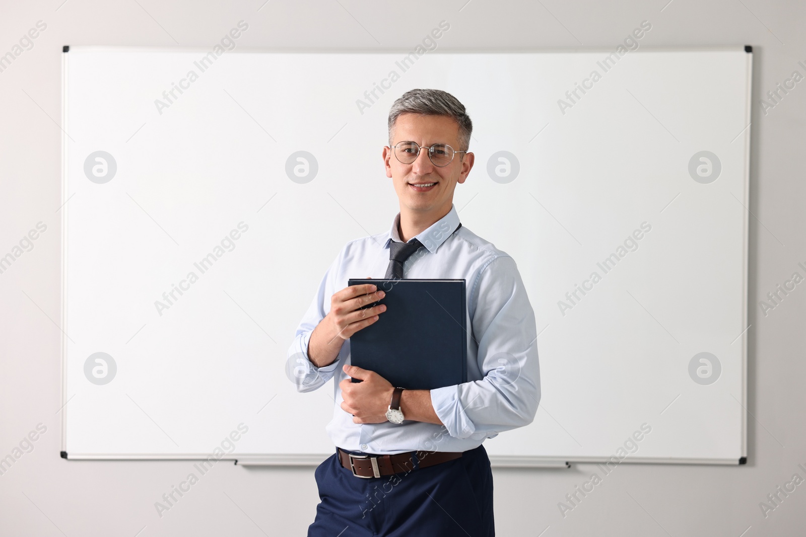 Photo of Teacher with notebook near whiteboard in classroom