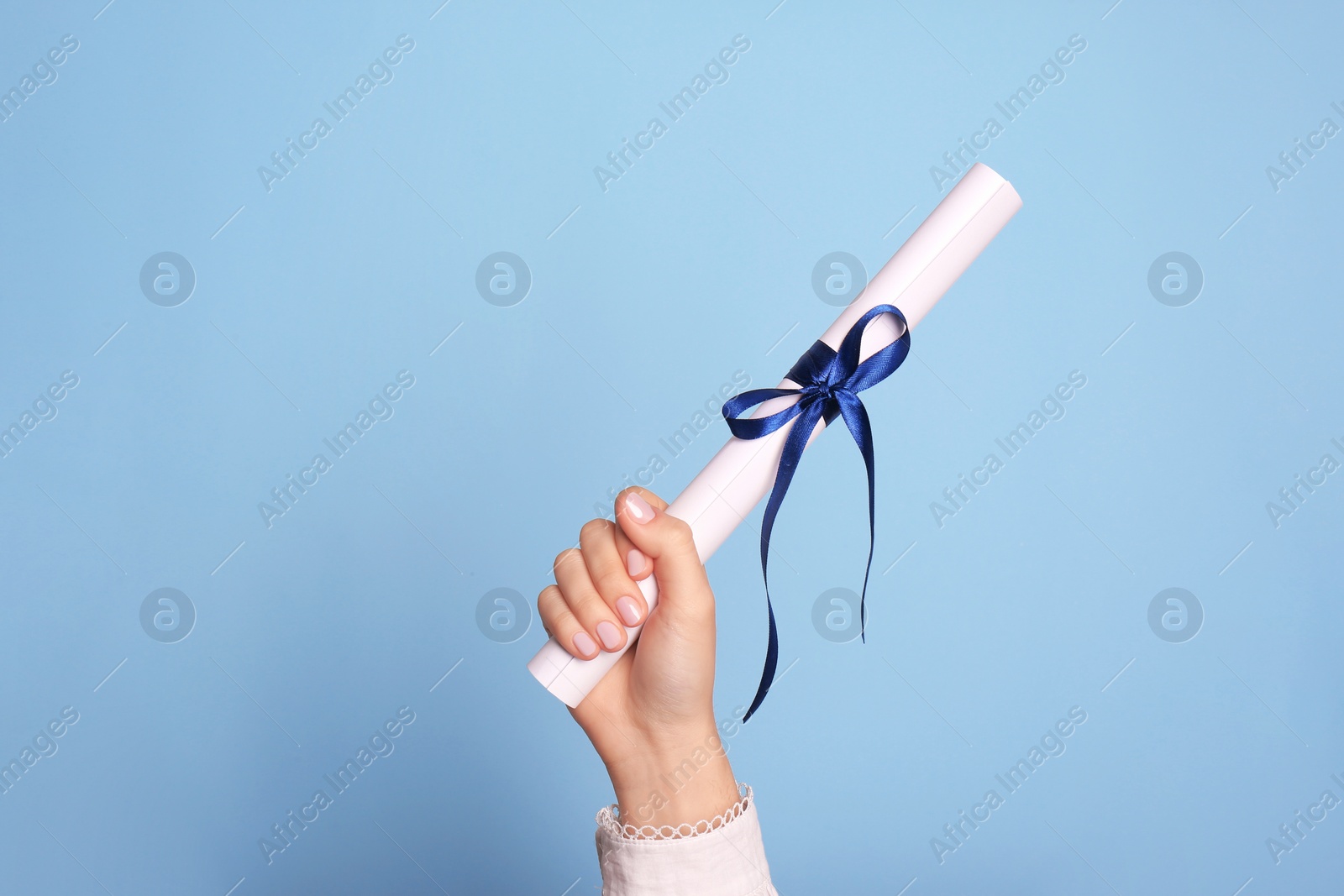 Photo of Student holding rolled diploma with ribbon on light blue background, closeup