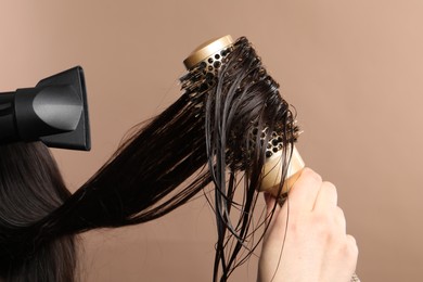 Photo of Hairdresser blow drying client's hair on light brown background, closeup