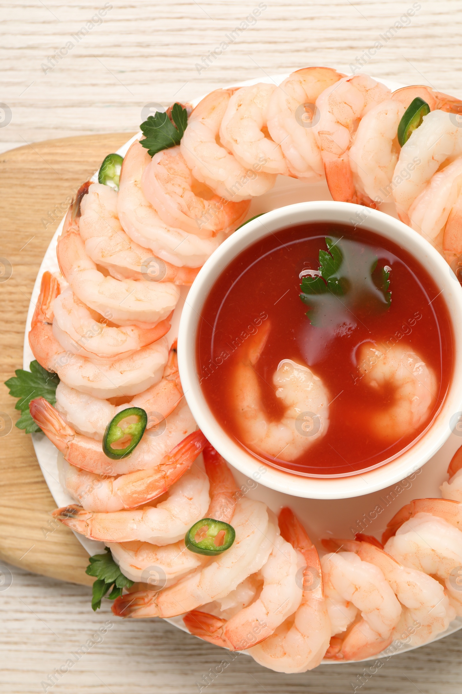 Photo of Tasty boiled shrimps with cocktail sauce, chili and parsley on light wooden table, top view