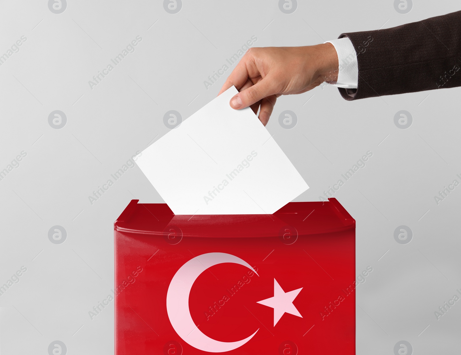 Image of Man putting his vote into ballot box decorated with flag of Turkey against light background, closeup