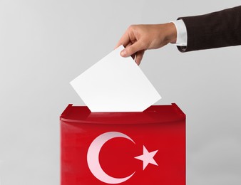 Man putting his vote into ballot box decorated with flag of Turkey against light background, closeup