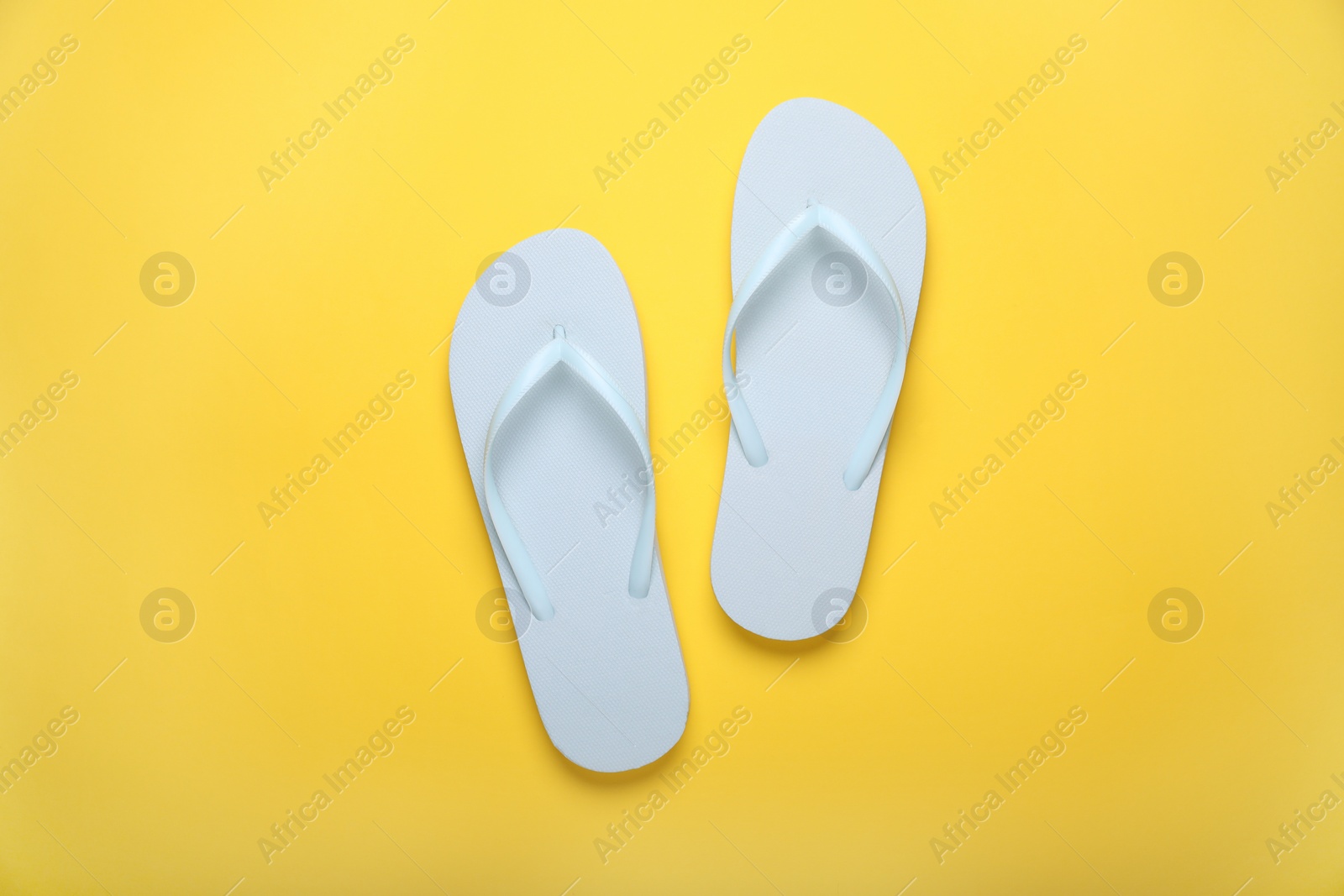 Photo of Stylish white flip flops on yellow background, top view