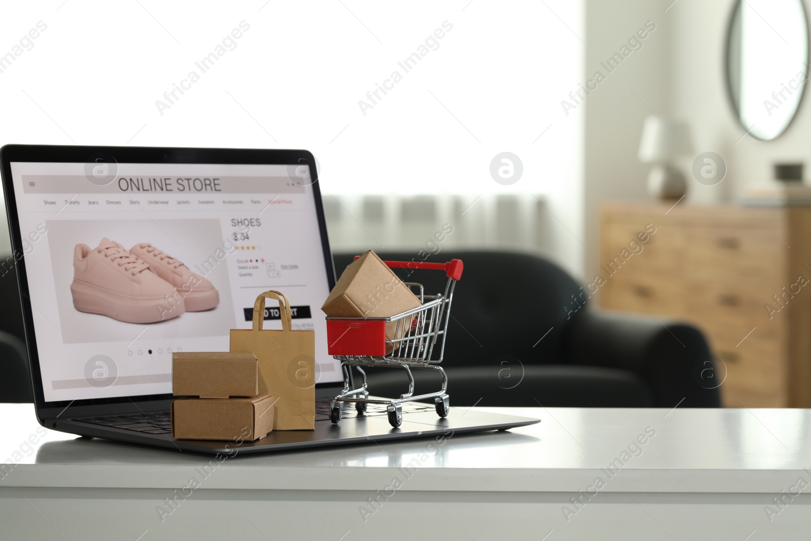Photo of Online store. Laptop, mini shopping cart and purchases on white table, space for text