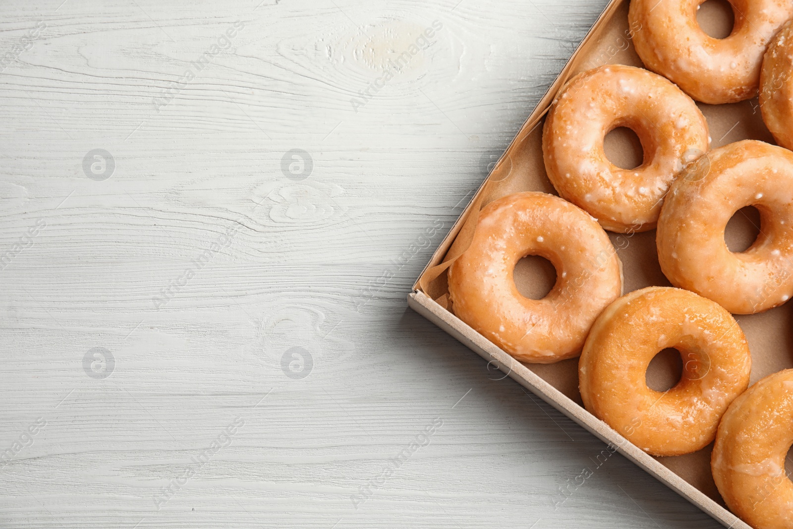 Photo of Delicious donuts on white wooden table, top view. Space for text