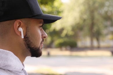 Photo of Young man with wireless headphones listening to music in park. Space for text