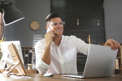 Photo of Freelancer talking on phone while working at table indoors