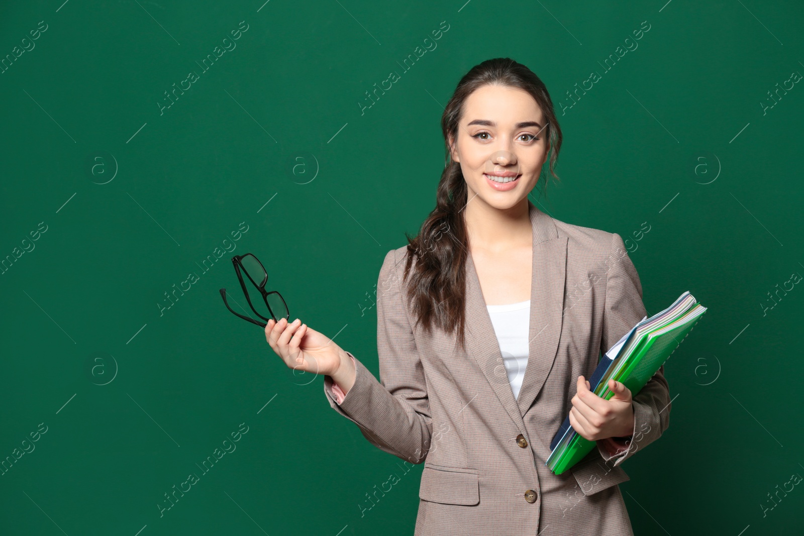 Photo of Portrait of beautiful young teacher with books near chalkboard, space for text
