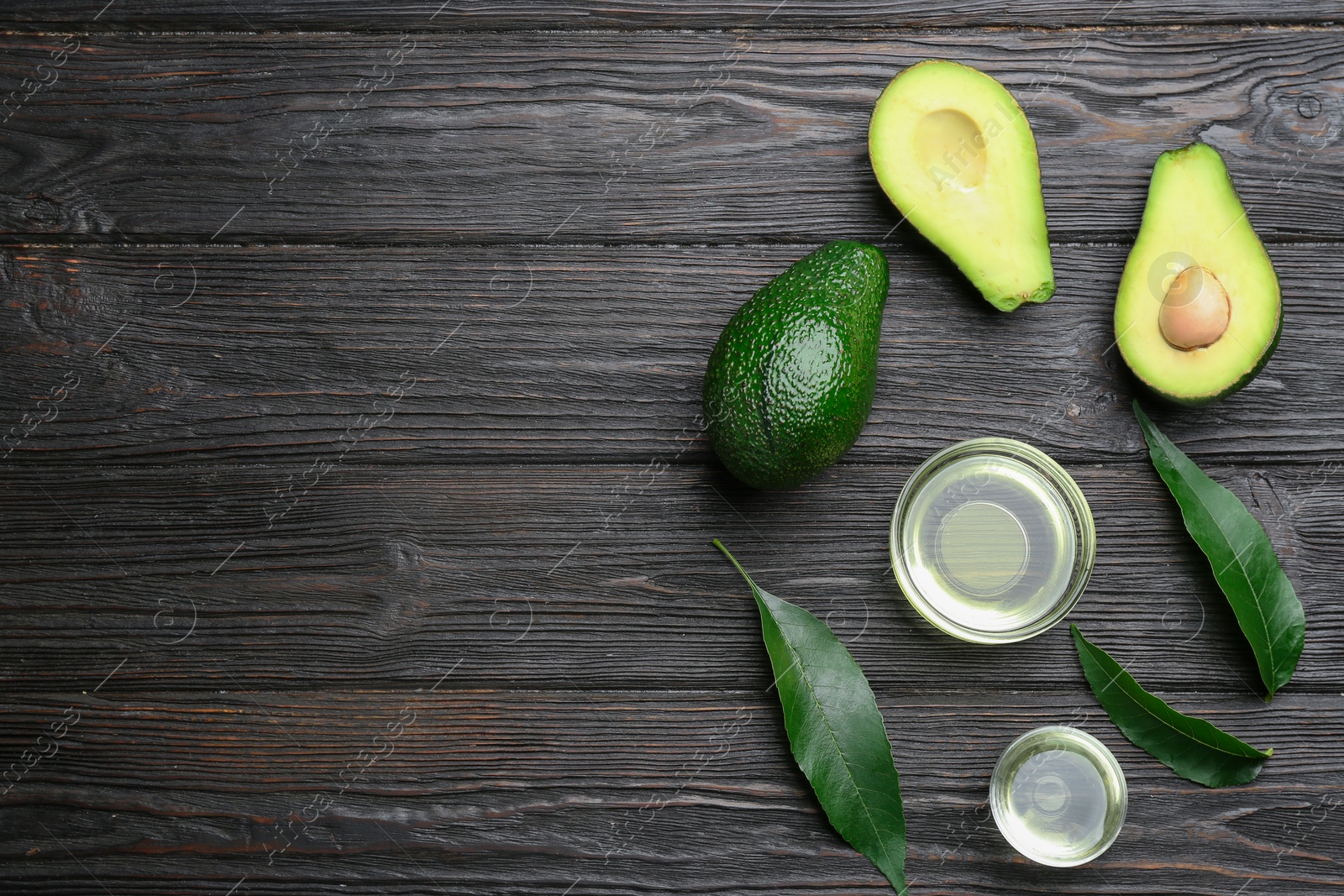 Photo of Bowls of natural oil and avocados on black wooden background, flat lay. Space for text