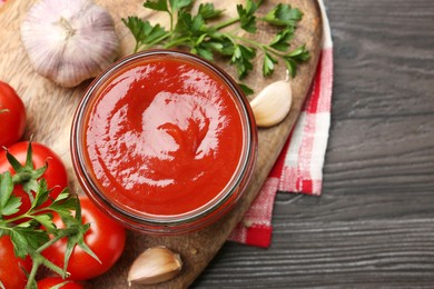 Photo of Tasty ketchup, fresh tomatoes, parsley and spices on grey wooden table, flat lay. Space for text