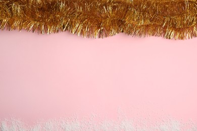 Photo of Shiny golden tinsel and snow on pink background, top view. Space for text