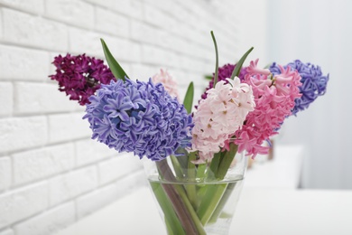 Photo of Beautiful hyacinths in glass vase on table against brick wall. Spring flowers