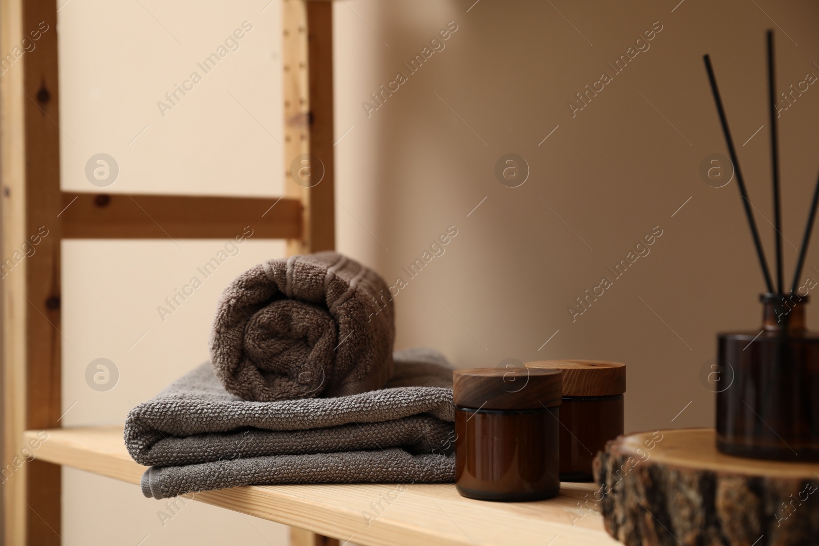 Photo of Soft towels, candles and air freshener on wooden shelf indoors, closeup
